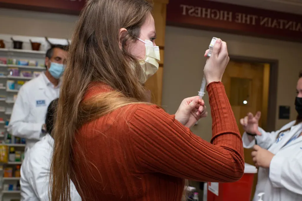 A pharmacy student preps a vaccine in a syringe